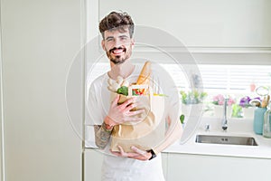 Young handsome man holding a paper bag full of fresh groceries at home