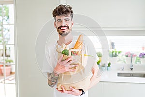 Young handsome man holding a paper bag full of fresh groceries at home