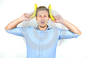 Young handsome man holding two fresh bananas near his head looking funny on isolated white background