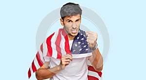 Young handsome man holding united states flag annoyed and frustrated shouting with anger, yelling crazy with anger and hand raised