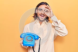 Young handsome man holding vintage telephone smiling happy doing ok sign with hand on eye looking through fingers