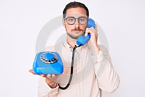 Young handsome man holding vintage telephone thinking attitude and sober expression looking self confident