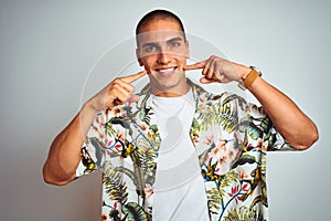 Young handsome man on holidays wearing Hawaiian shirt over white background smiling cheerful showing and pointing with fingers