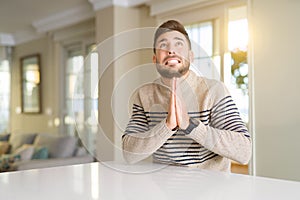 Young handsome man at home begging and praying with hands together with hope expression on face very emotional and worried