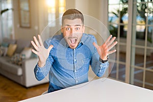 Young handsome man at home very happy and excited, winner expression celebrating victory screaming with big smile and raised hands