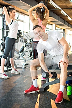 Young handsome man lifting weights with friends in the background.