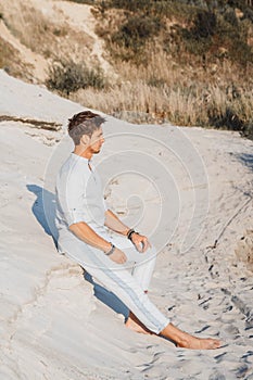 Young handsome man in light clothing sits in the desert. Concept of freedom relaxation. Place for text or advertising