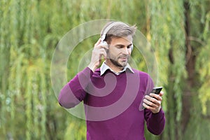 young handsome man listen music in headphones and chating on smartphone outdoor