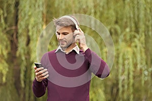 young handsome man listen music in headphones and chating on smartphone outdoor