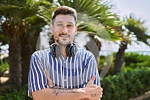 Young handsome man listening to music using headphones outdoors happy face smiling with crossed arms looking at the camera