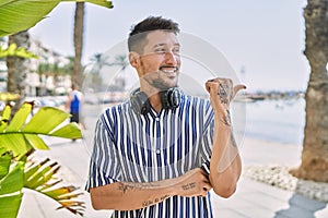 Young handsome man listening to music using headphones outdoors smiling with happy face looking and pointing to the side with