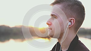 Young handsome man listens to music on beach during sunset. slow motion. lens flare effects