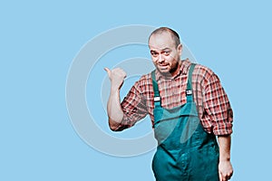 Young, handsome man look at camera in coveralls pointing with hands empty space,