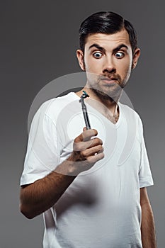 Young handsome man looking at shaver over grey background.