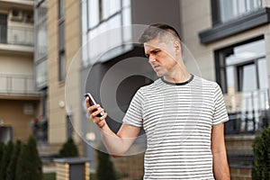 Young handsome man manager in a fashionable striped t-shirt with a stylish hairstyle stands with a mobile phone in hands