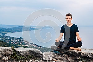 Young handsome man in a meditative position sits on a lawn on a background of forest and sunset. Concept of freedom relaxation.