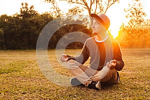 Young handsome man in a meditative position sits on a lawn on a background of forest and sunset. Concept of freedom relaxation.