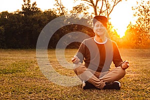 Young handsome man in a meditative position sits on a lawn on a background of forest and sunset. Concept of freedom relaxation.