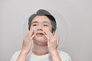 Young handsome man with moisturizer on his face, isolated on gray background. Skin care concept