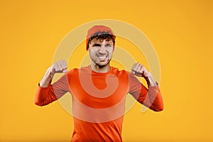 Young handsome man in orange hat stands in winning position, self-defense concept, boxing, on isolated yellow background