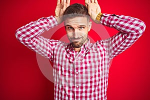 Young handsome man over red isolated background Doing bunny ears gesture with hands palms looking cynical and skeptical