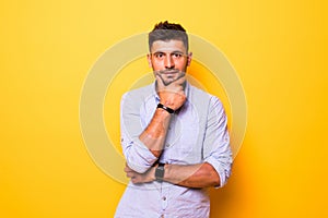 Young handsome man over yellow isolated background looking confident at the camera smiling with crossed arms and hand raised on