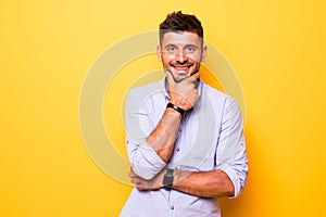 Young handsome man over yellow isolated background looking confident at the camera smiling with crossed arms and hand raised on