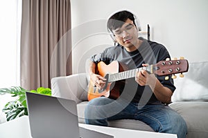 Young handsome man playing acoustic guitar sitting on the sofa in the living room at home