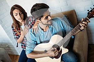 Young handsome man playing guitar while his girlfriend is singing