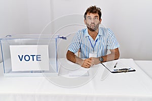 Young handsome man at political election sitting by ballot making fish face with lips, crazy and comical gesture