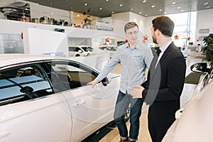 Young handsome man preparing to buy new car in auto dealership.