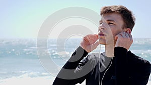 Young handsome man puts the earphones on before run workout standing on the beach