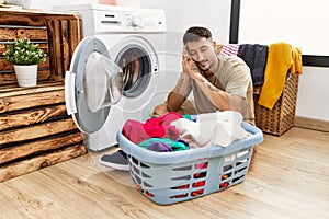 Young handsome man putting dirty laundry into washing machine sleeping tired dreaming and posing with hands together while smiling