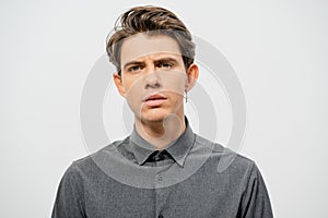 Young handsome man with a questioning face studio portrait. Boy style, trendy grey shirt look with cool hairstyle