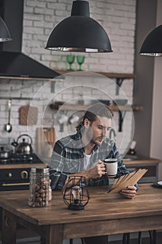 Young handsome man reading old letters at his kitchen