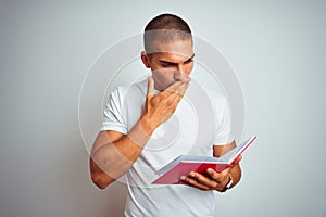 Young handsome man reading red book over white isolated background cover mouth with hand shocked with shame for mistake,