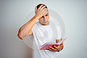 Young handsome man reading red book over white isolated background stressed with hand on head, shocked with shame and surprise