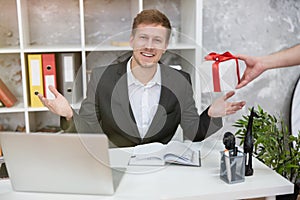 Young handsome man recieved unexpectable decorated with red bow present from his colleague at his working place in office looking