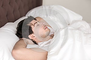 Young handsome man resting alone in bed with eyes closed