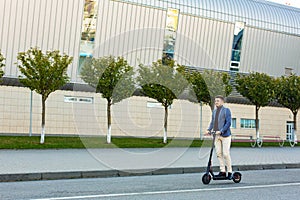 Young handsome man riding the e-scooter on the road near the airport on the sunset. Trendy urban transportation on