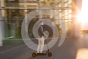 Young handsome man riding the e-scooter on the road near the airport on the sunset. Trendy urban transportation on