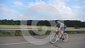 Young handsome man riding at vintage bicycle in the country road. Sporty guy cycling at the track. Male cyclist riding