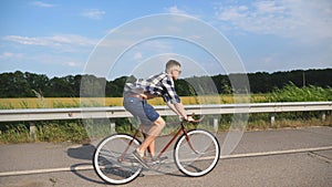Young handsome man riding at vintage bicycle in the country road. Sporty guy cycling at the track. Male cyclist riding