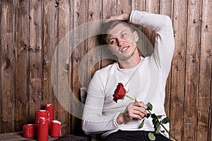 Young handsome man with a rose in his hands sitting near wood wall