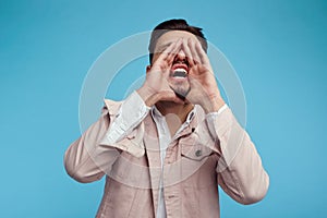Young handsome man screaming with hand near mouth on blue studio background