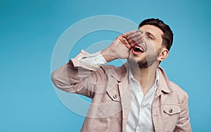 Young handsome man screaming with hand near mouth on blue studio background