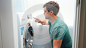 Young handsome man setting washing machine in bathroom. Male doing laundry and housework