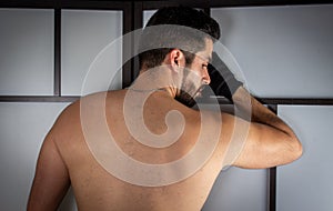 Young handsome man shirtless leaning against the wall with his back to the camera