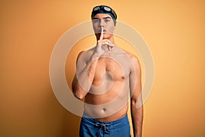 Young handsome man shirtless wearing swimsuit and swim cap over isolated yellow background asking to be quiet with finger on lips