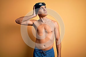 Young handsome man shirtless wearing swimsuit and swim cap over isolated yellow background confuse and wondering about question